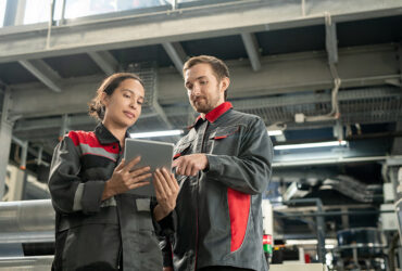 Two young quality control managers of polymer processing factory using tablet Two young quality control managers of contemporary polymer processing factory looking at touchpad display while looking through data
